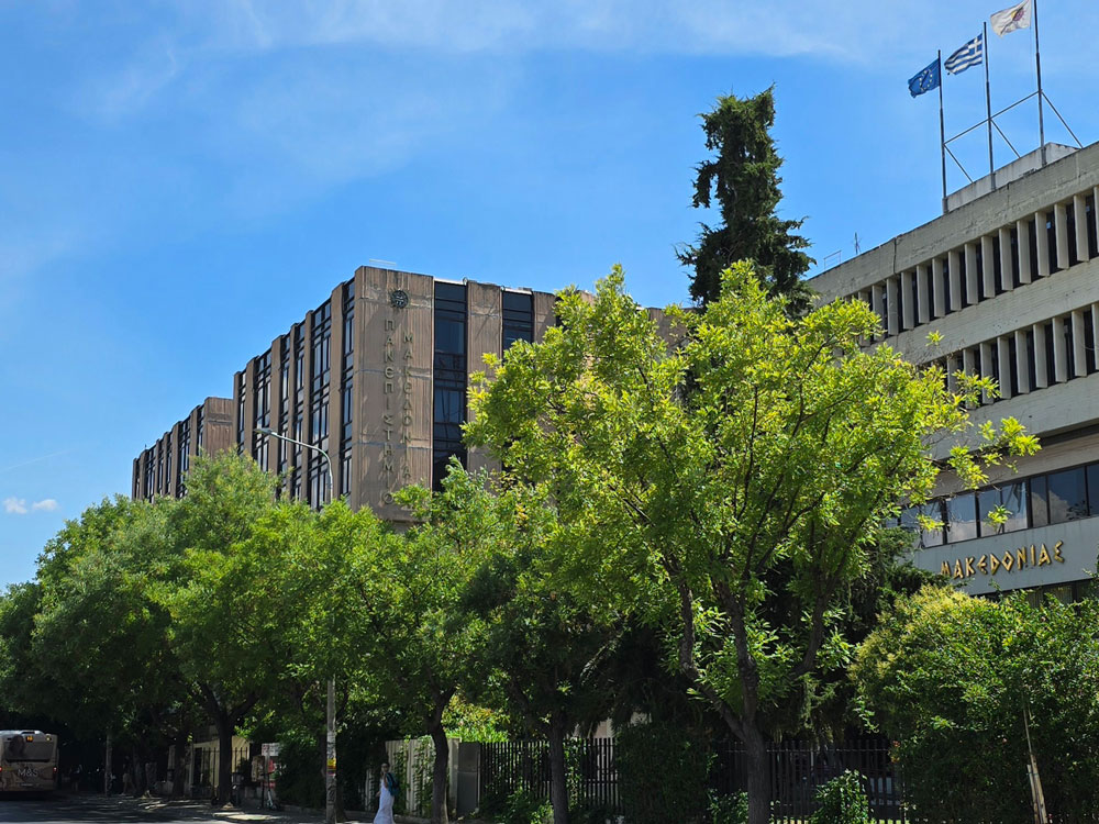 The square main building of the University of Macedonia, hidden behind green trees