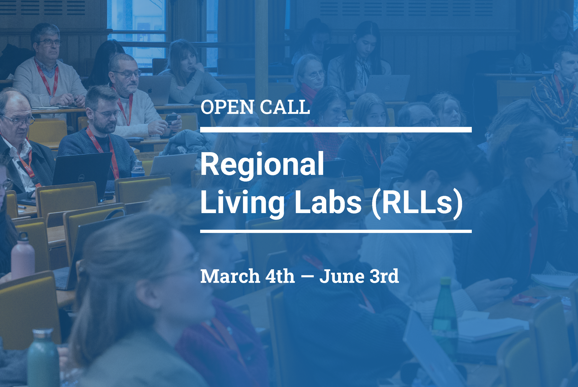 2026_RLL Open Call_Banner-Website Blue-tinted banner image of a conference or lecture hall filled with seated attendees, many using laptops and wearing red lanyards. Overlaid white text reads: “OPEN CALL” at the top, “Regional Living Labs (RLLs)” in large bold letters in the center, and “March 4th – June 3rd” at the bottom, separated by thin horizontal lines.