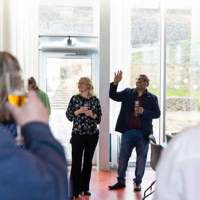 Two people speak to participants during a gathering in a bright room.