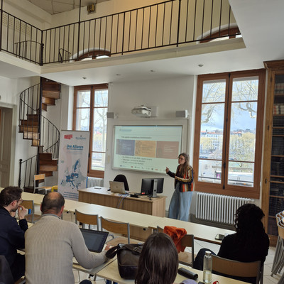 A presenter discusses a slide during a BAUHAUS4EU meeting in a spacious classroom.