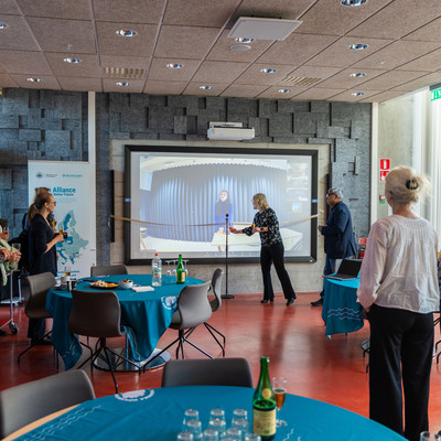 Two people stand in front of a large screen showing an online connection during a BAUHAUS4EU event.