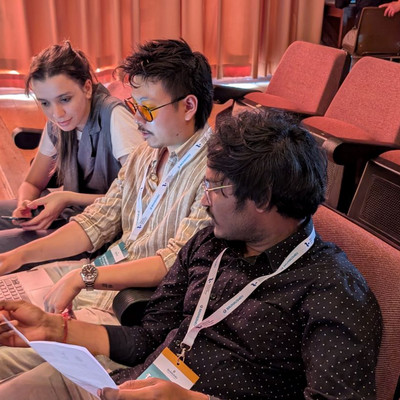 Three students are sitting in a confeence room next to each other. They are looking and pointing at a laptop screen that the student in the middle is holding.