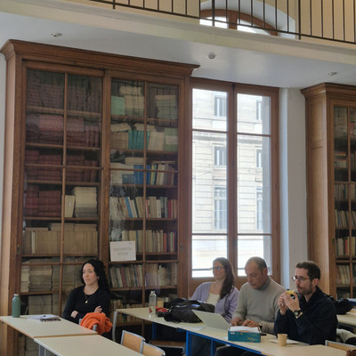 Workshop participants sit at tables in front of tall bookcases filled with books.
