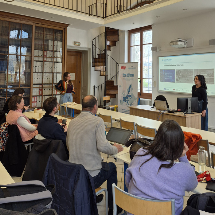 A presenter discusses a slide during a BAUHAUS4EU meeting in a spacious classroom.