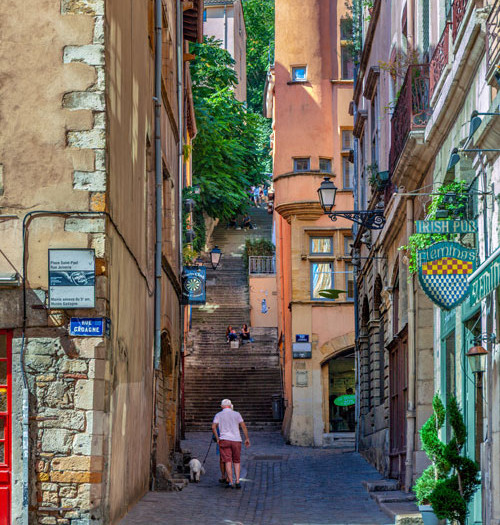 Old cobbled alleyway in Lyon with a staircase and a man walking his dog