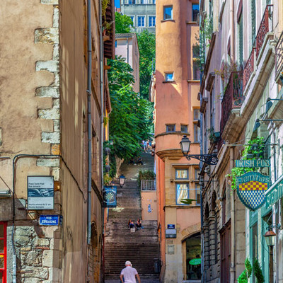 Old cobbled alleyway in Lyon with a staircase and a man walking his dog