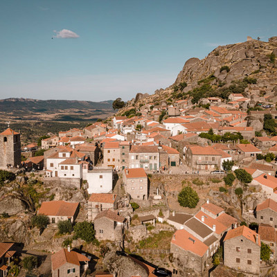 A historic village with stone houses red-tiled roofs is nestled among large boulders on a rocky hillside.